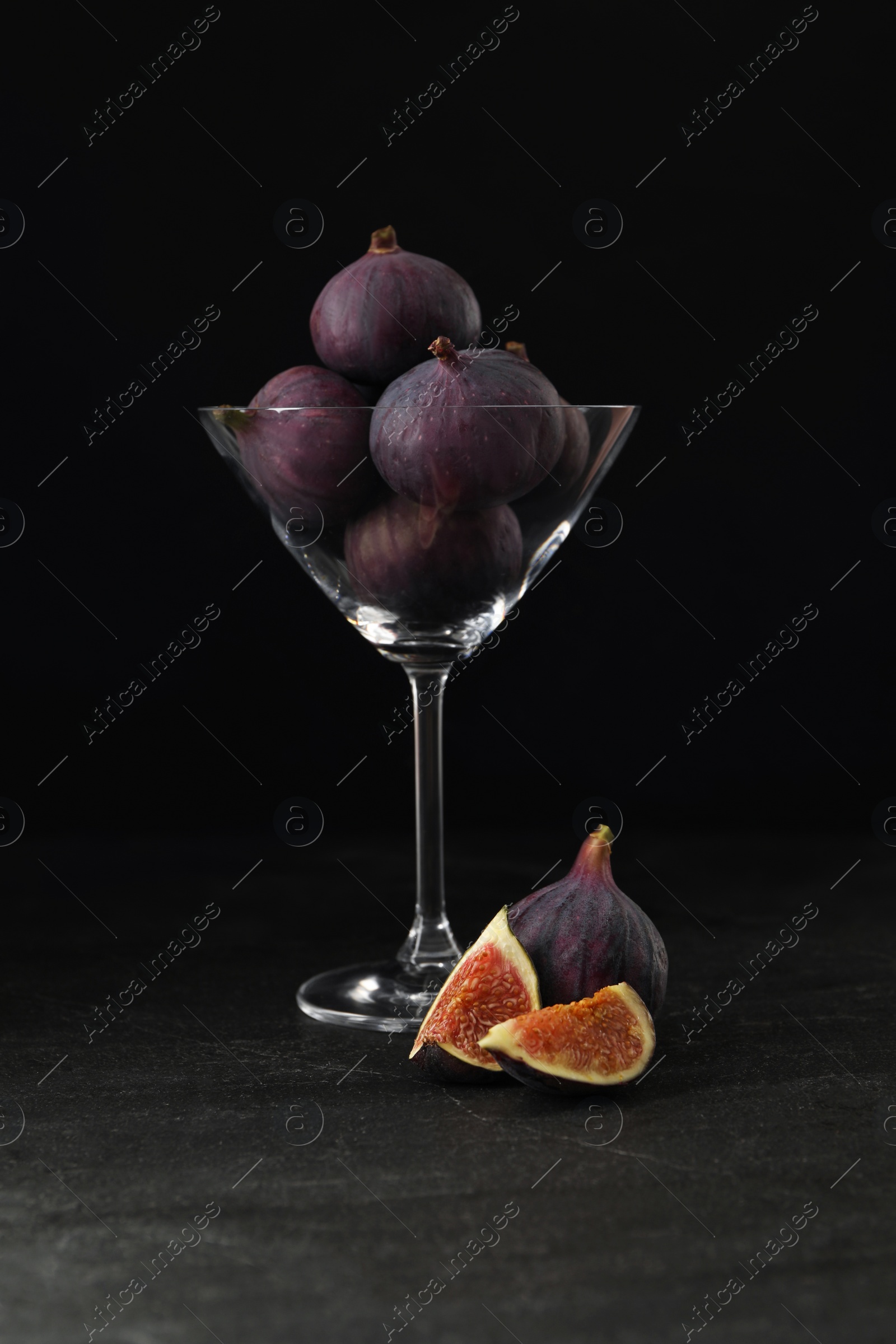 Photo of Tasty raw figs in martini glass on black table