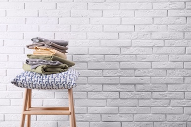 Stack of clean bed sheets and pillow on stool near white brick wall. Space for text