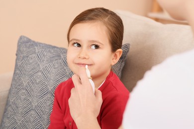 Mother using nasal spray to treat her little daughter on sofa indoors, closeup