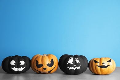 Photo of Pumpkins with scary faces on table against color background, space for text. Halloween decor