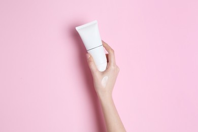 Woman holding tube of cream on pink background, closeup