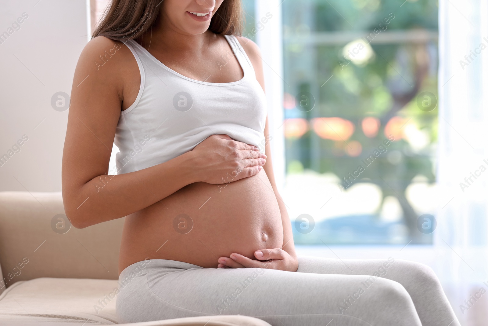 Photo of Pregnant woman sitting on sofa at home, closeup