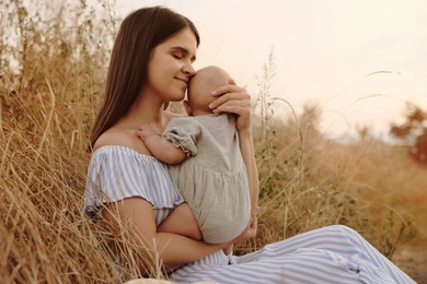 Happy mother with little baby in field at sunset