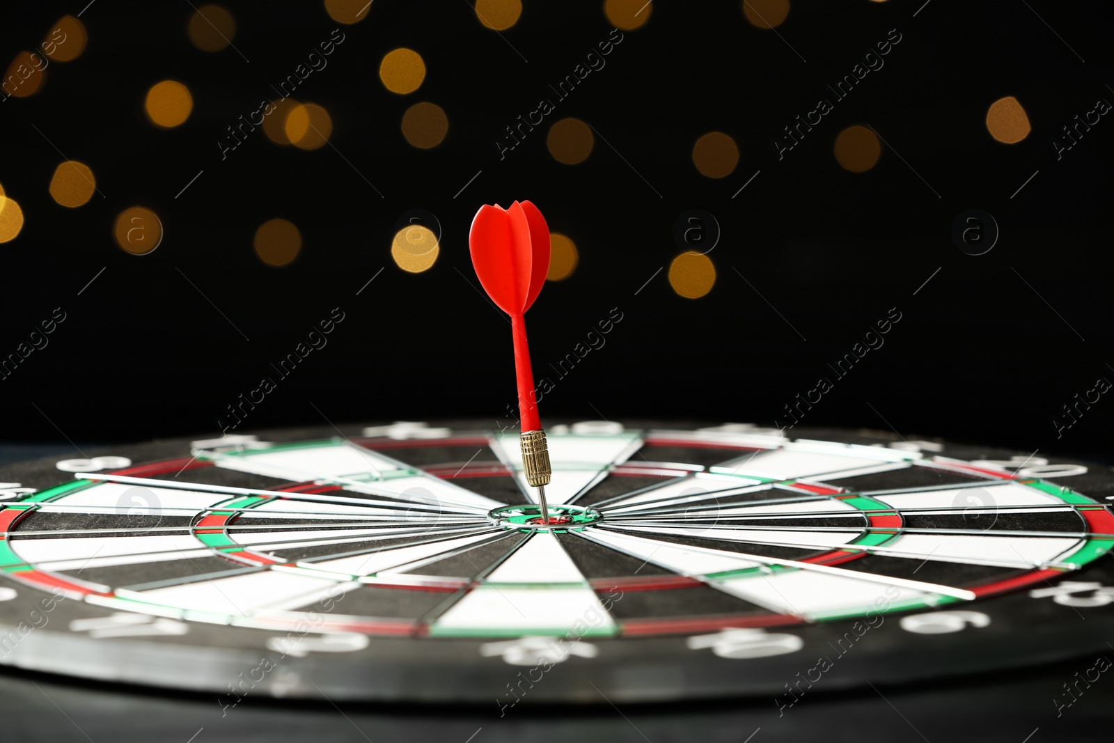 Photo of Red arrow hitting target on dart board against blurred lights