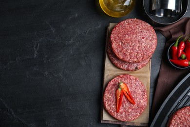 Photo of Raw hamburger patties with chili pepper on black table, flat lay. Space for text