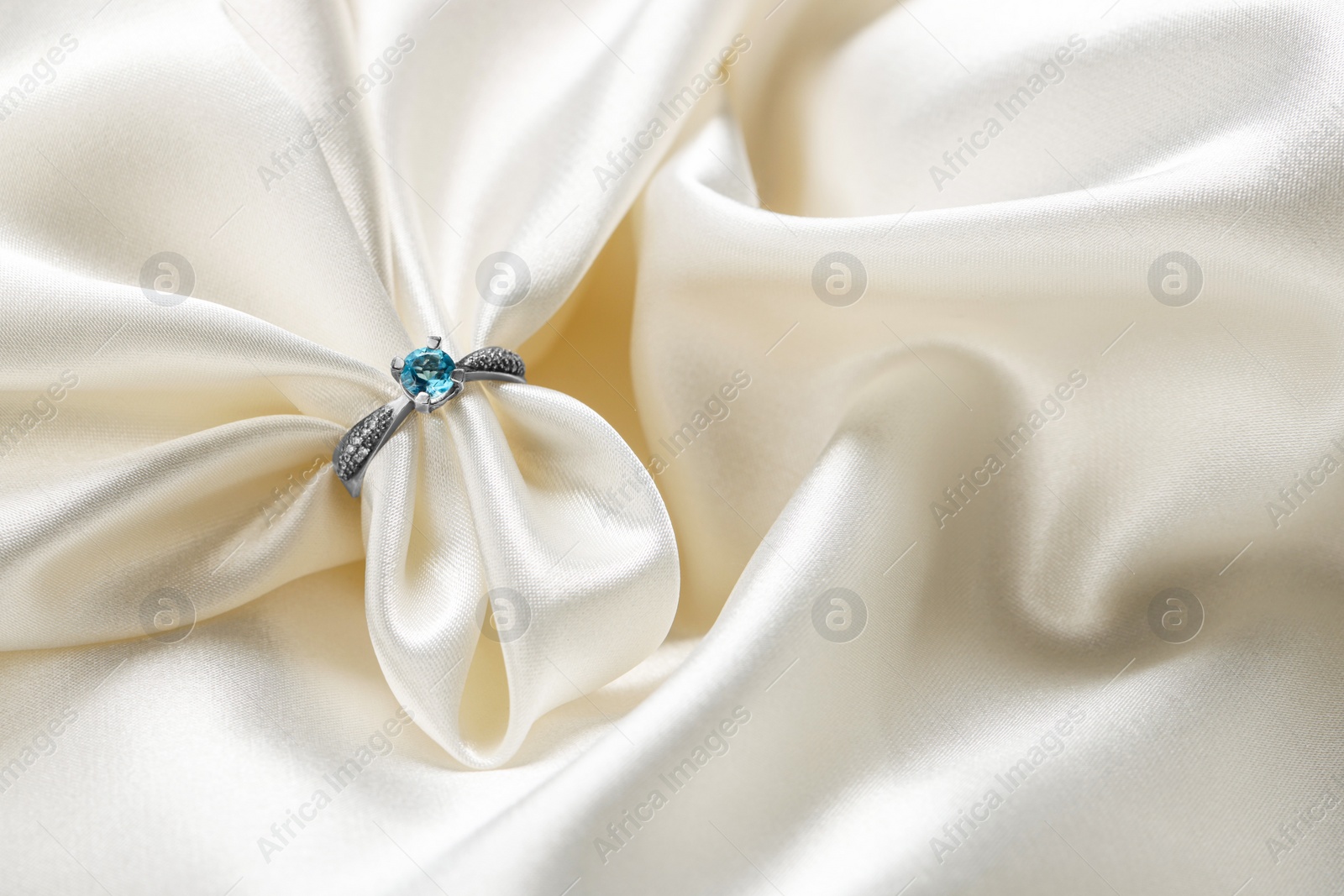 Photo of Beautiful ring with light blue gemstone on white fabric, space for text. Luxury jewelry