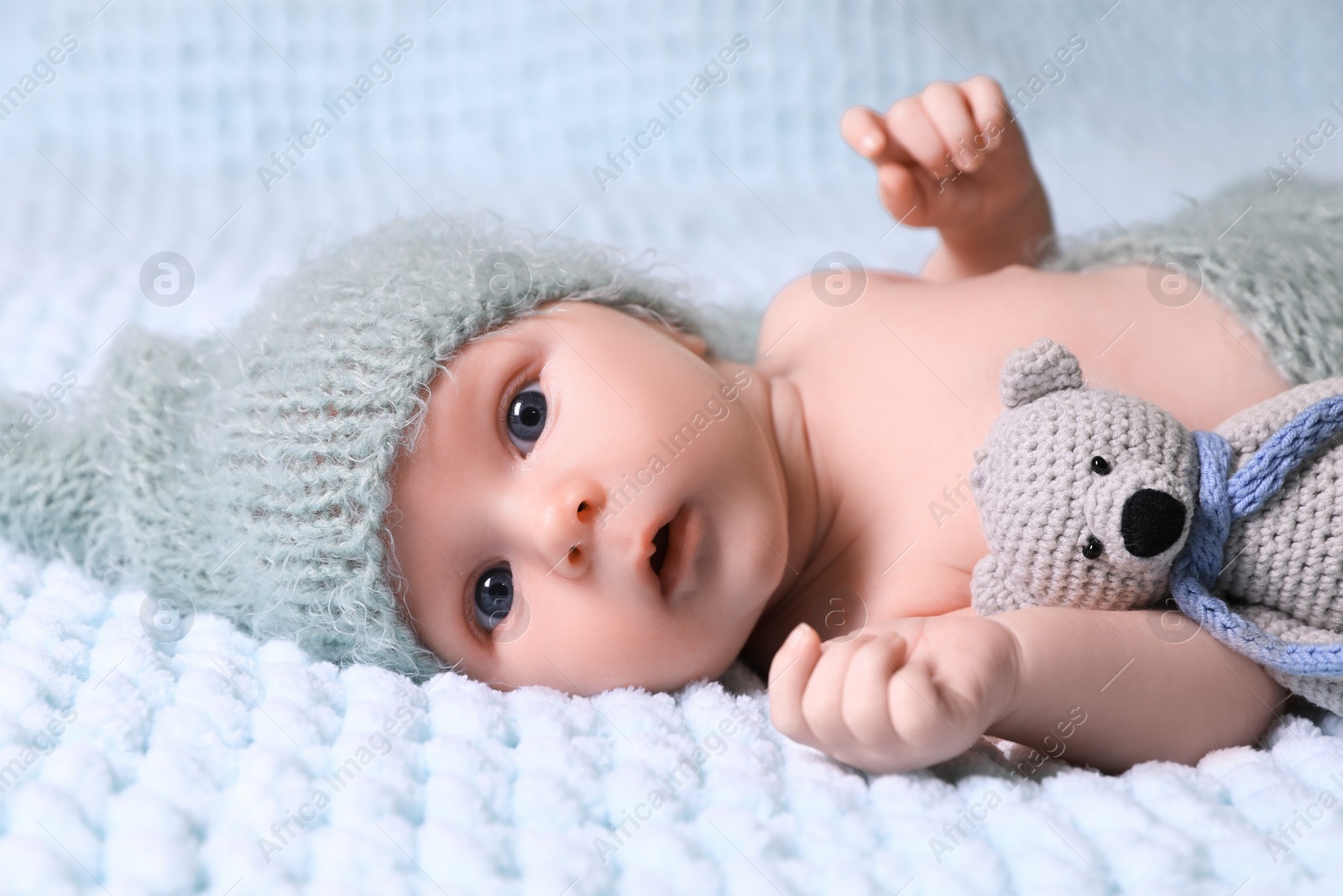 Photo of Cute newborn baby with crochet toy on light blue blanket