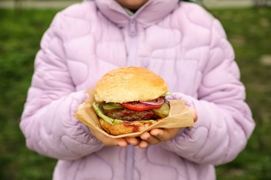 Photo of Little girl holding fresh delicious burger outdoors, closeup. Street food