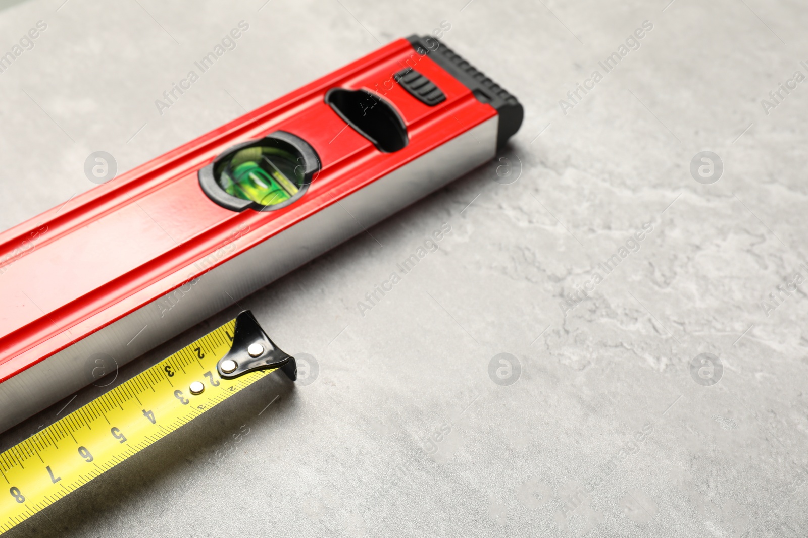 Photo of Building level and tape measure on grey table. Space for text