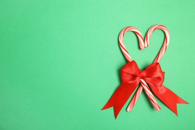 Photo of Heart shape made of tasty candy canes with bow on color background, top view. Space for text