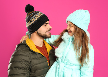 Photo of Happy father and daughter in warm clothes on pink background. Winter vacation