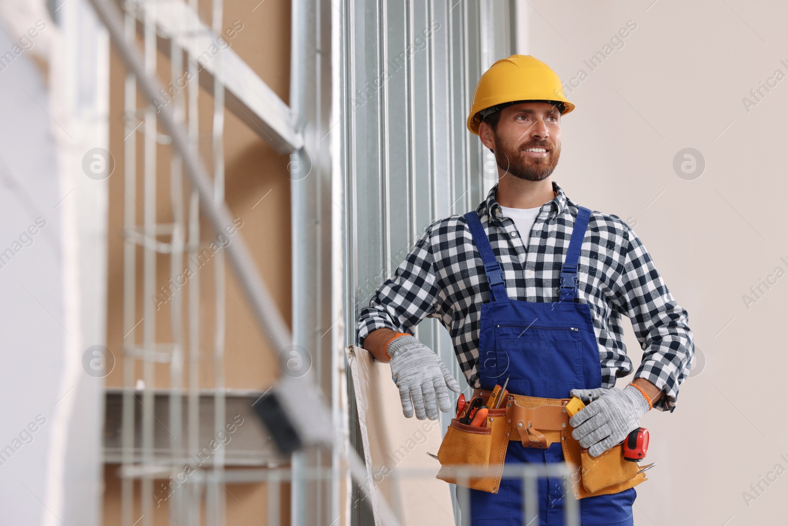 Photo of Professional builder in uniform with tool belt indoors