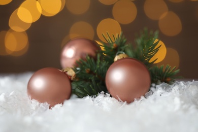 Beautiful Christmas balls and fir branch on snow against blurred festive lights