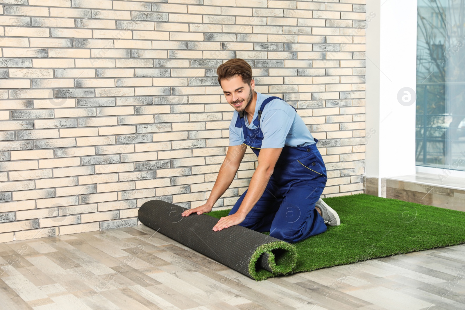 Photo of Man rolling out artificial grass carpet indoors. Space for text