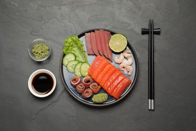 Tasty salmon slices, shrimp, cucumber, soy sauce and tuna on black table, flat lay. Delicious sashimi dish
