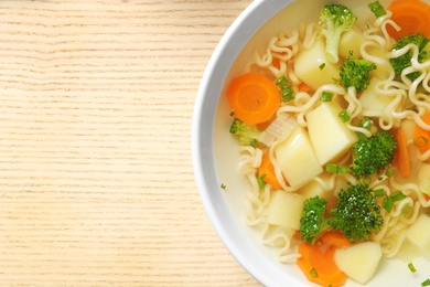 Bowl of fresh homemade vegetable soup on wooden background, top view. Space for text