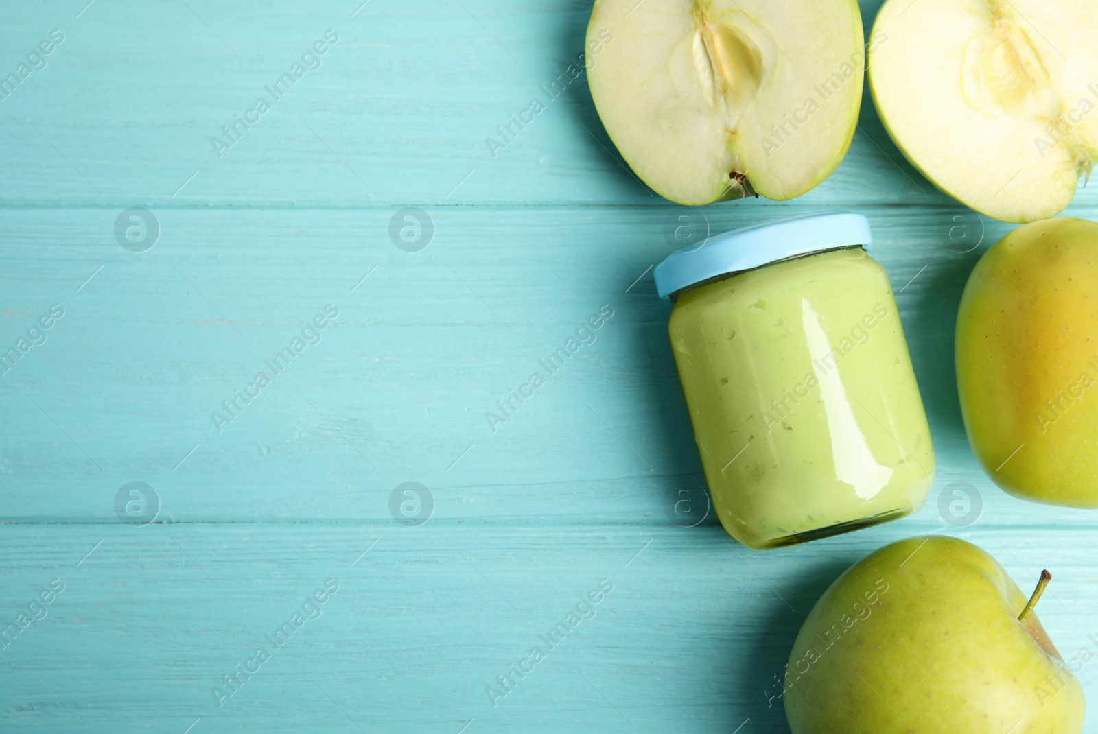 Photo of Jar with baby food and fresh apples on light blue wooden table, flat lay. Space for text