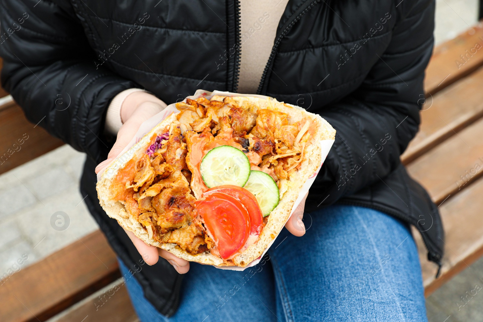 Photo of Woman holding delicious bread with roasted meat and vegetables outdoors, closeup. Street food