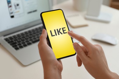 Image of Woman using smartphone with word Like on screen at table, closeup