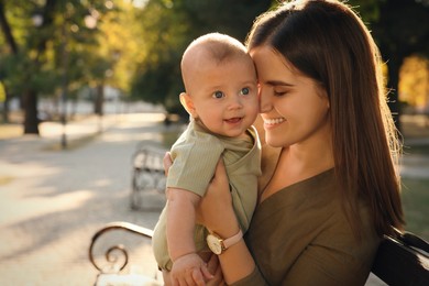 Young mother with her cute baby on bench in park