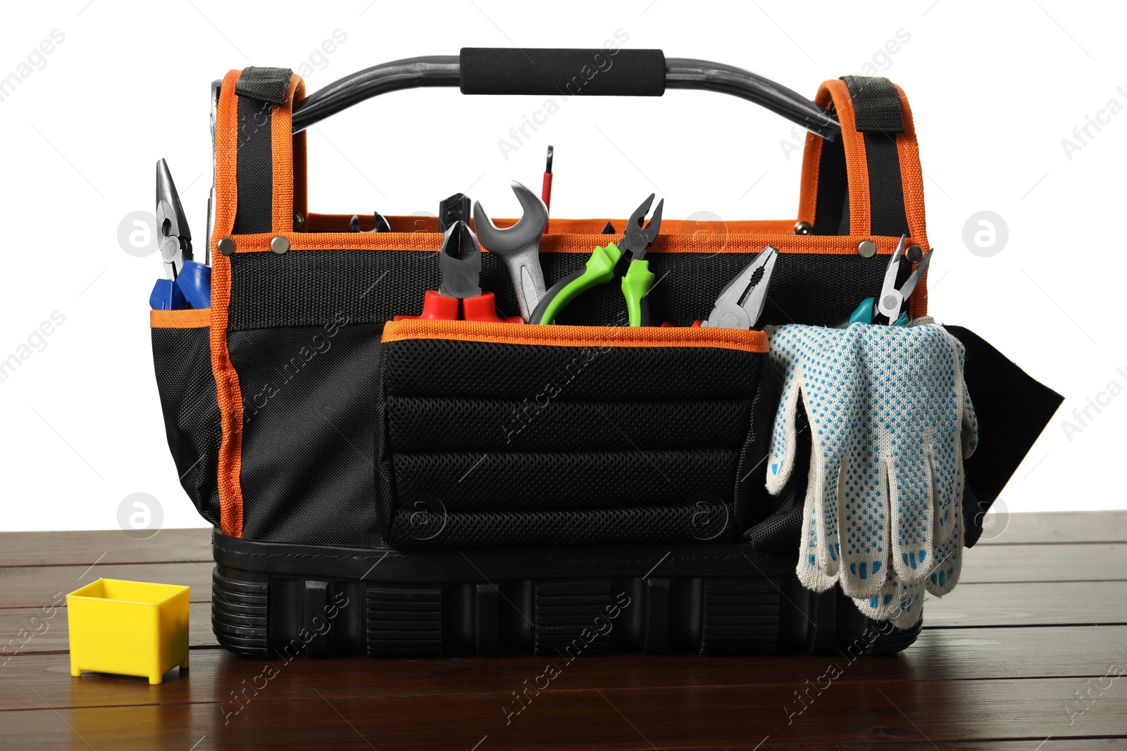 Photo of Tool bag with different pliers, work gloves and wrench on wooden table against white background