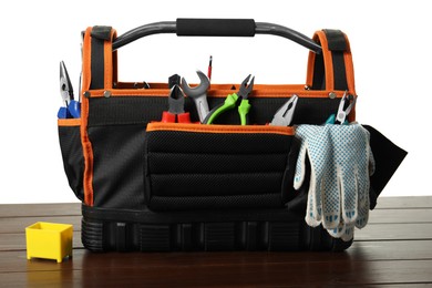 Tool bag with different pliers, work gloves and wrench on wooden table against white background