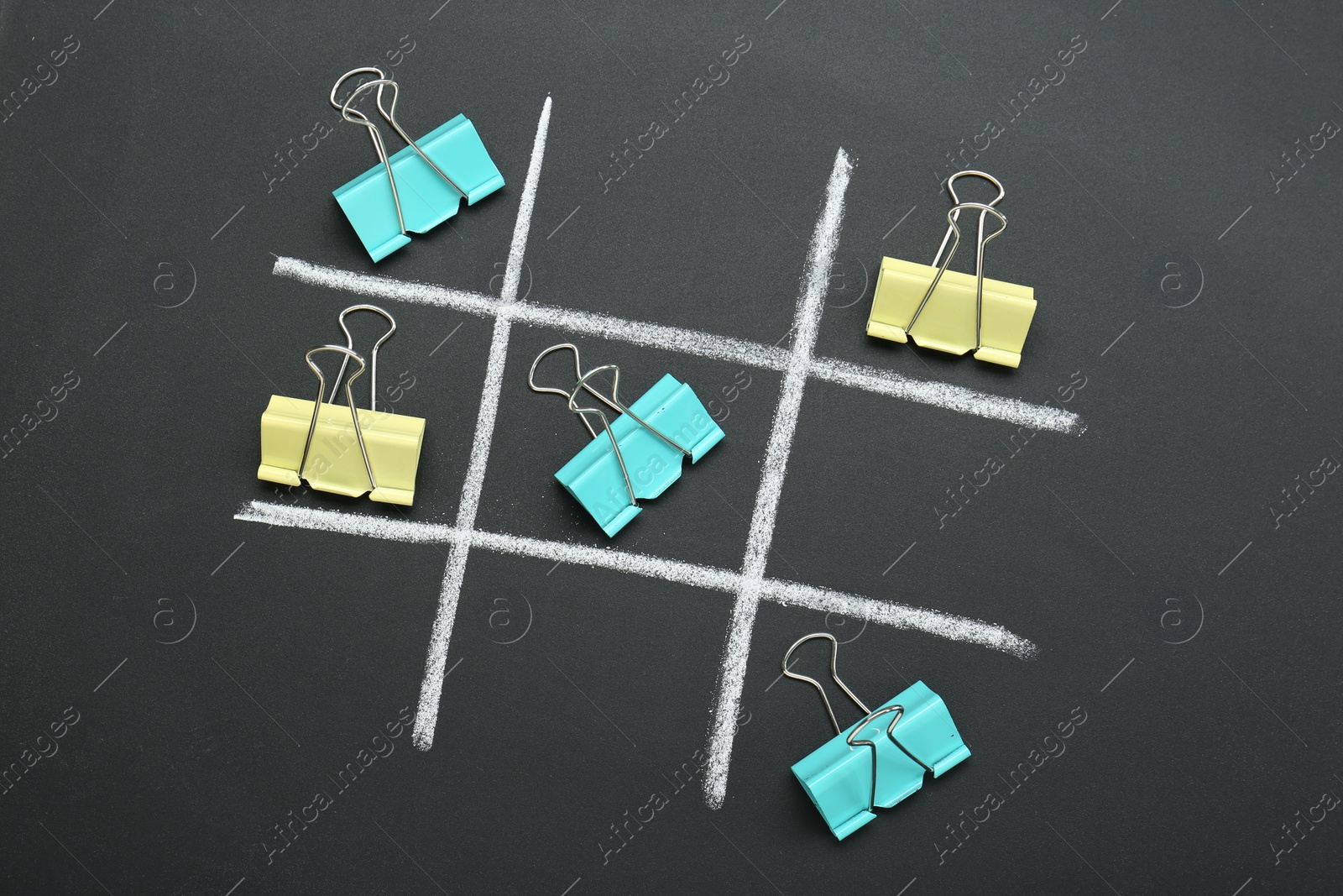 Photo of Tic tac toe game made with paper clips on chalkboard, top view