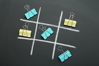 Tic tac toe game made with paper clips on chalkboard, top view