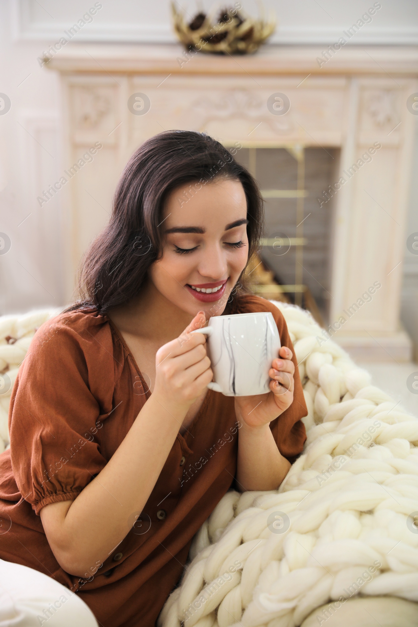 Photo of Woman with hot drink resting in comfortable papasan chair at home