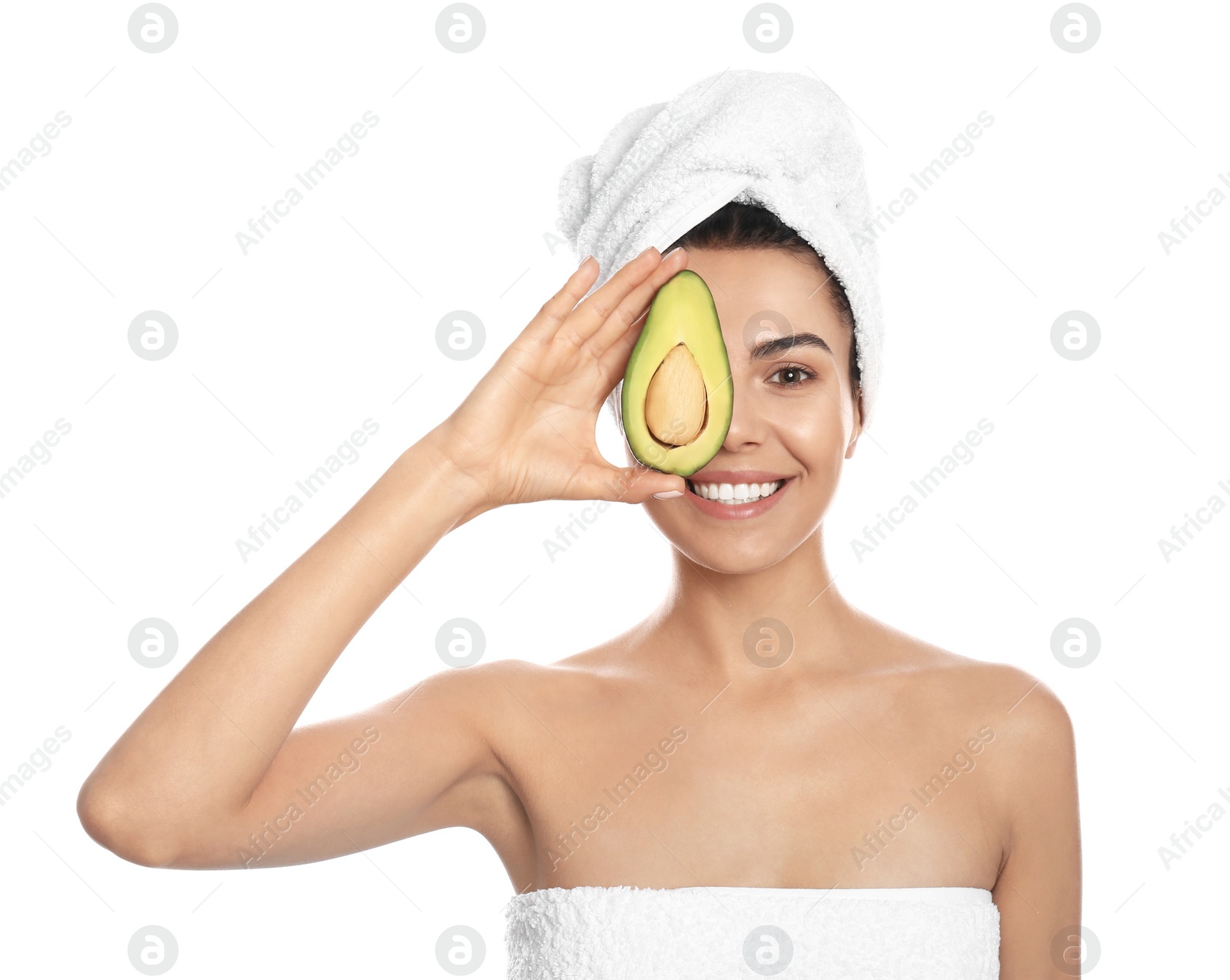 Photo of Happy young woman with towel holding avocado on white background. Organic face mask