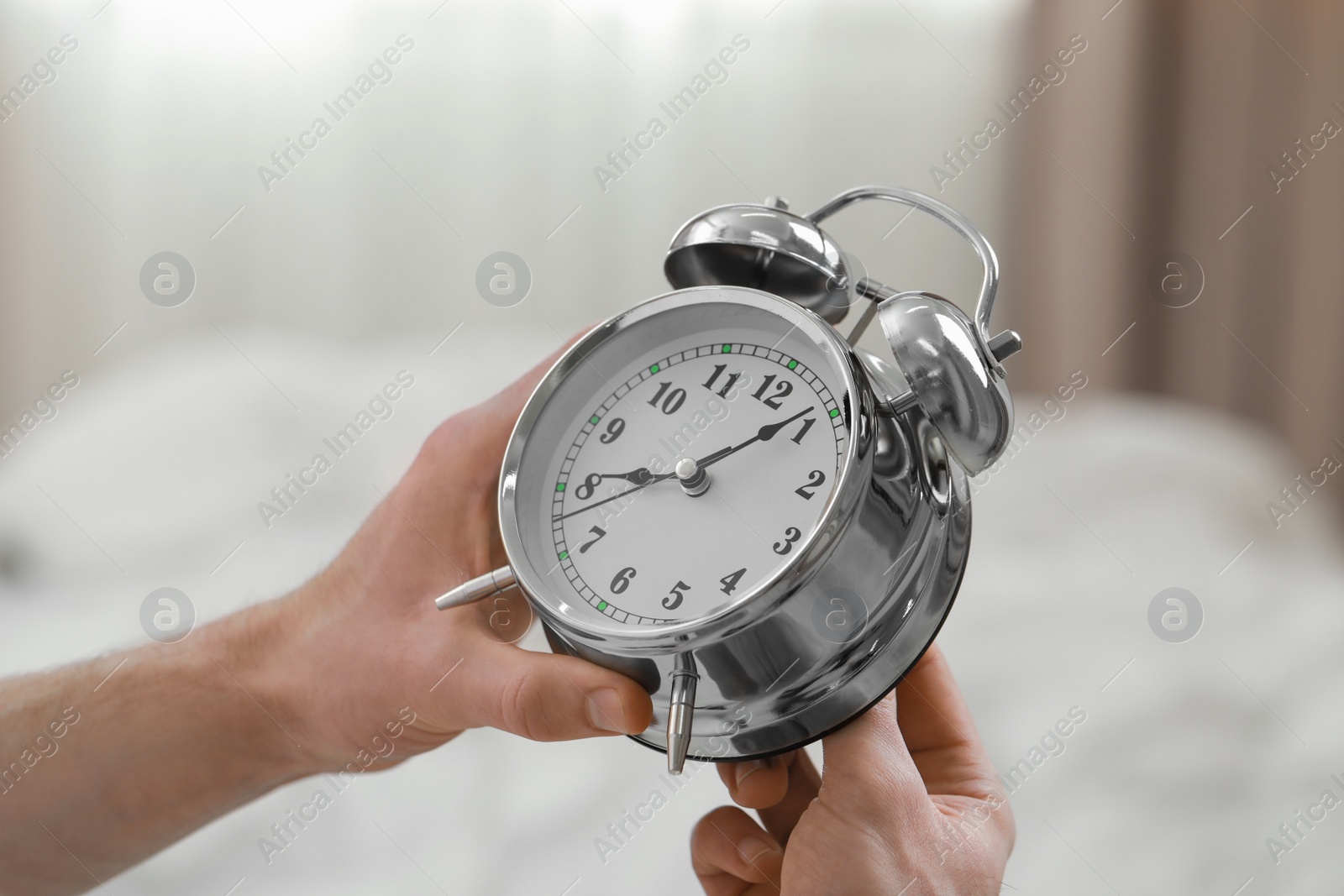 Photo of Man with alarm clock in bedroom, closeup of hands