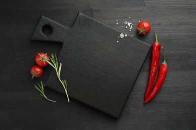 Photo of Cutting board, rosemary, chili peppers and tomatoes on black wooden table, flat lay. Space for text