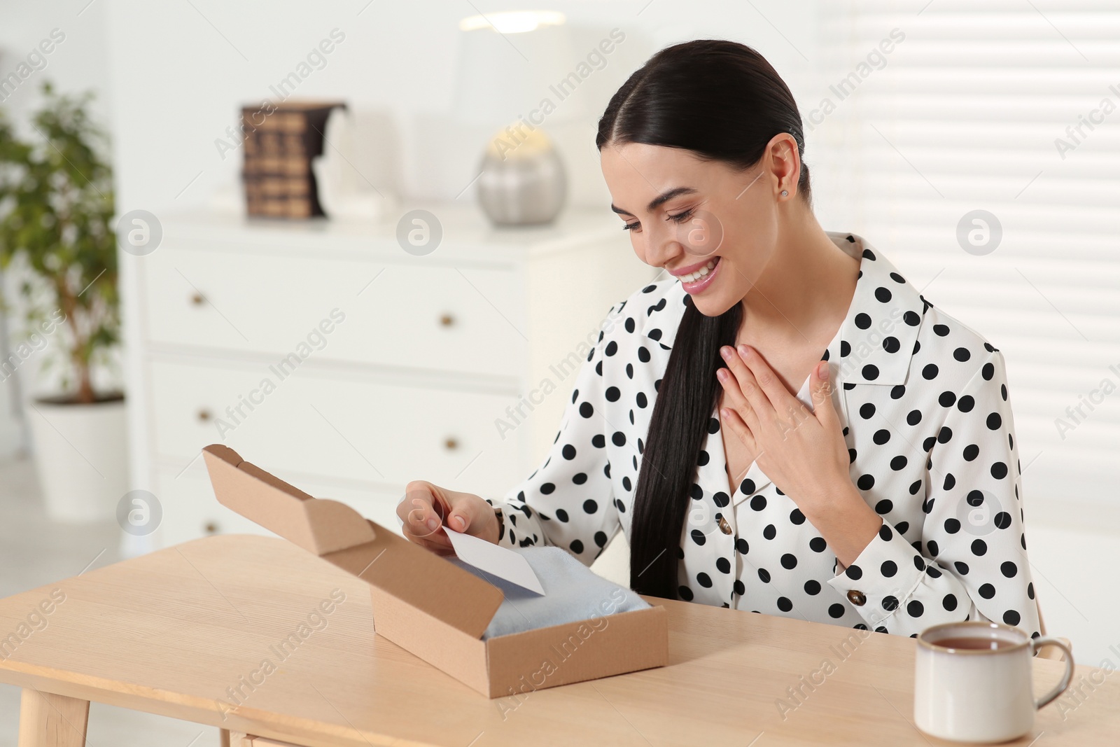 Photo of Happy woman holding greeting card near parcel with Christmas gift at home