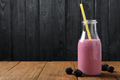 Bottle of blackberry smoothie with straw and berries on wooden table, space for text