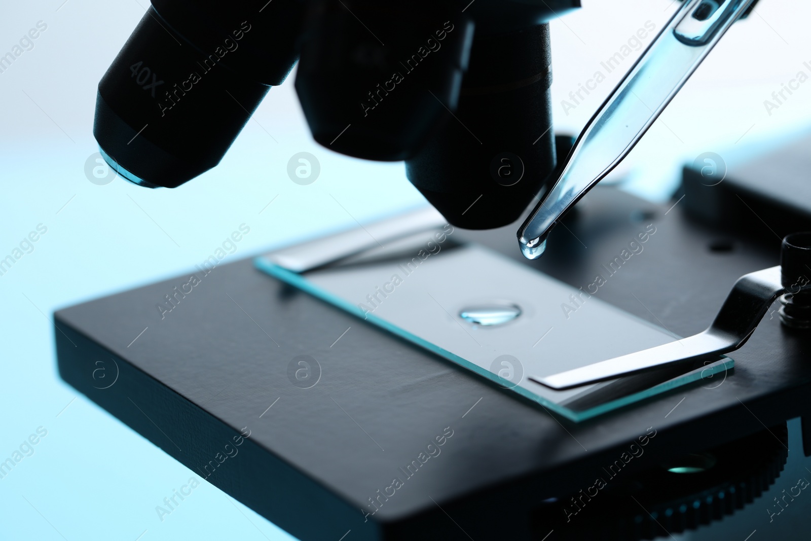 Photo of Dripping liquid from pipette onto glass slide on microscope at table, closeup