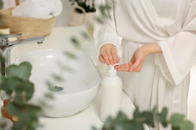 Young woman using body cream in bathroom, closeup