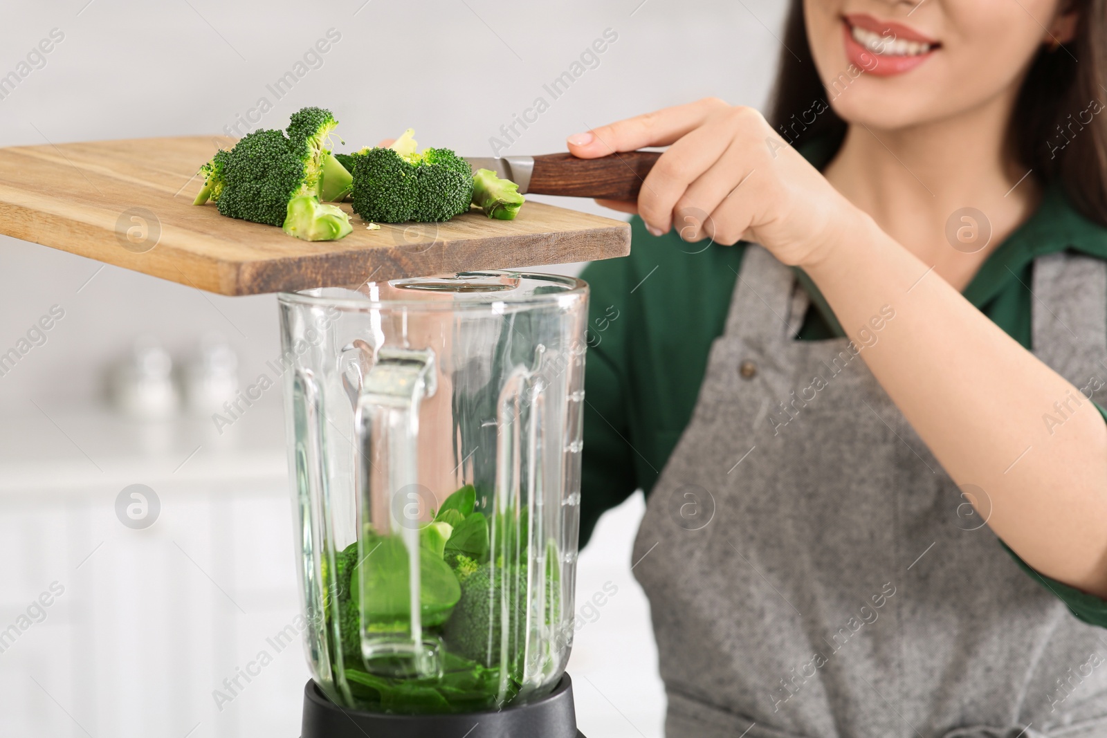 Photo of Woman adding broccoli into blender with ingredients for smoothie in kitchen, closeup