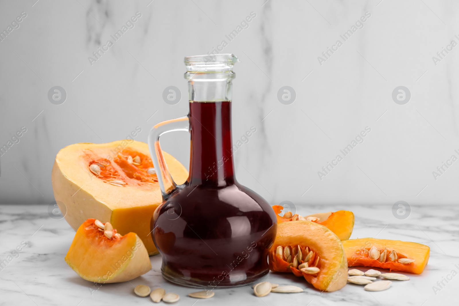 Photo of Fresh pumpkin seed oil in glass jug on white marble table