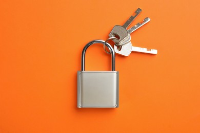 Photo of Modern padlock with keys on orange background, top view