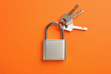 Modern padlock with keys on orange background, top view