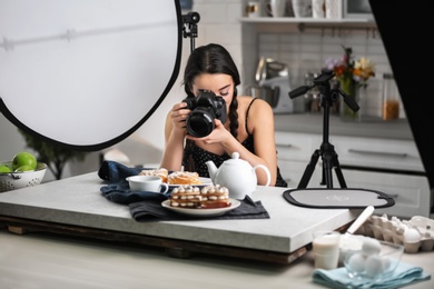 Young woman with professional camera taking food photo in studio