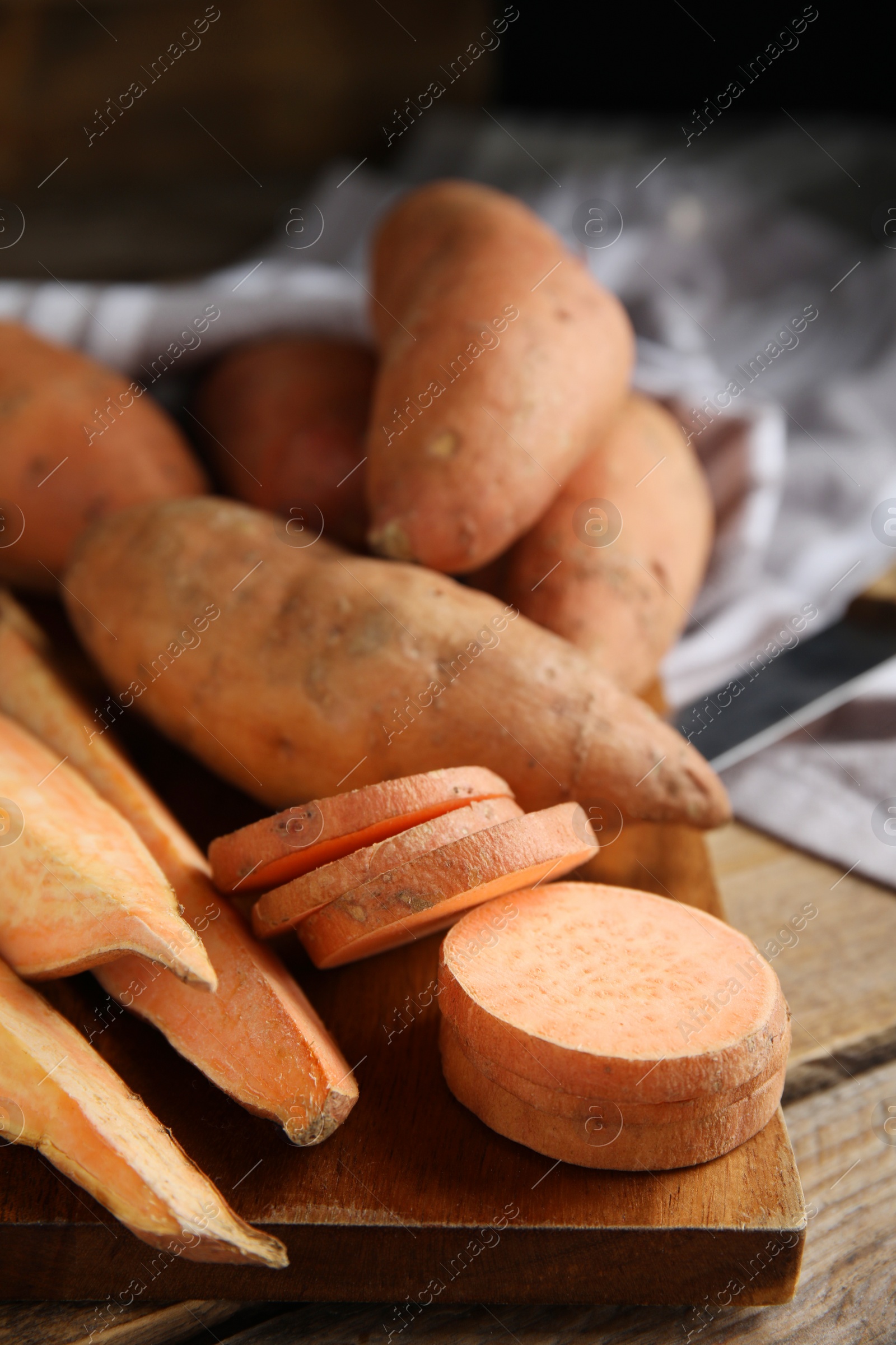 Photo of Wooden board with cut and whole sweet potatoes on table, closeup