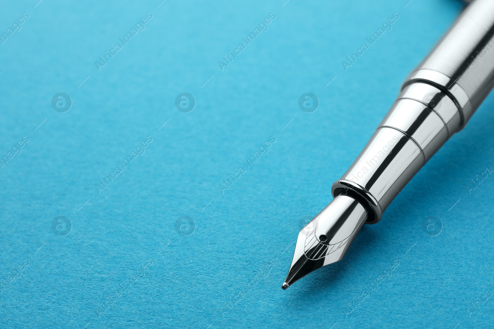 Photo of Stylish silver fountain pen on light blue background, closeup. Space for text