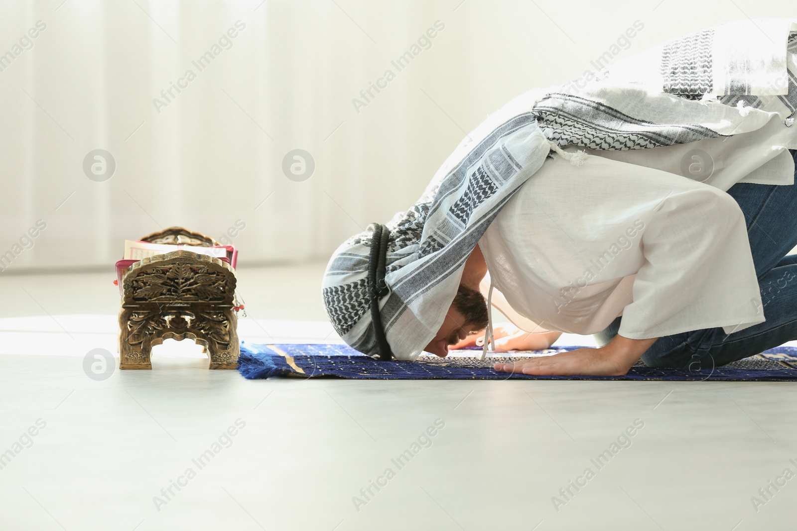 Photo of Muslim man in traditional clothes praying on rug indoors