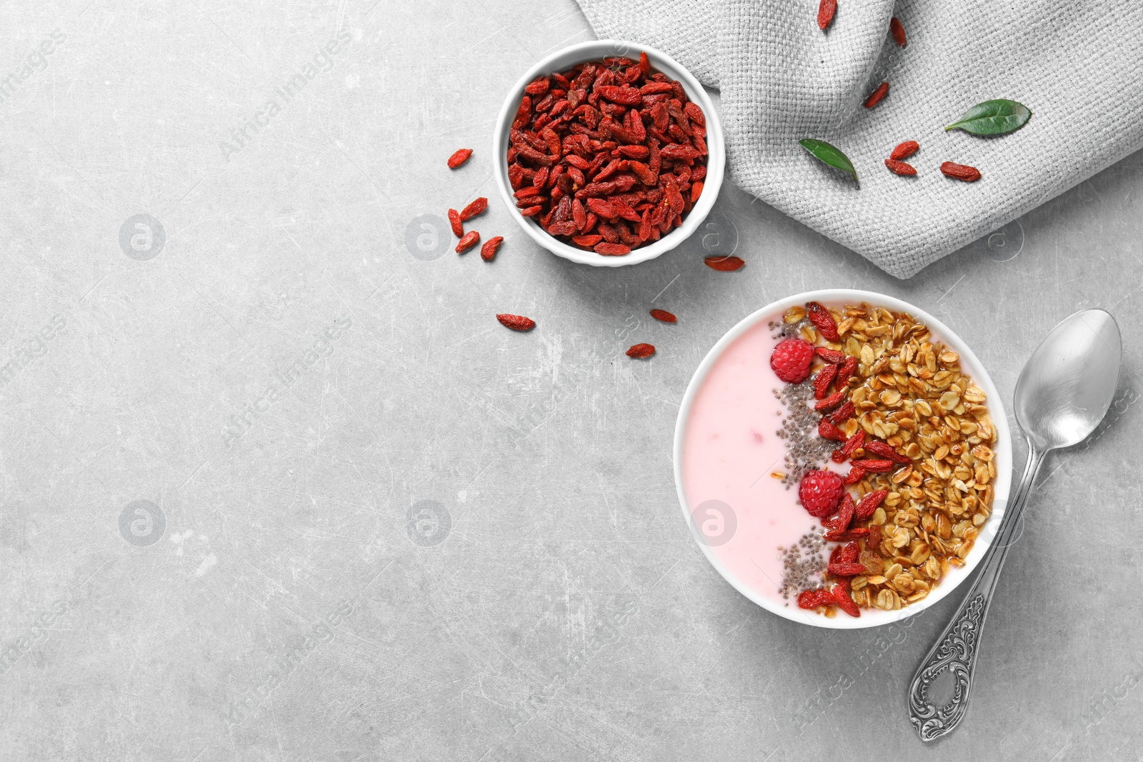 Photo of Smoothie bowl with goji berries and spoon on grey table, flat lay. Space for text