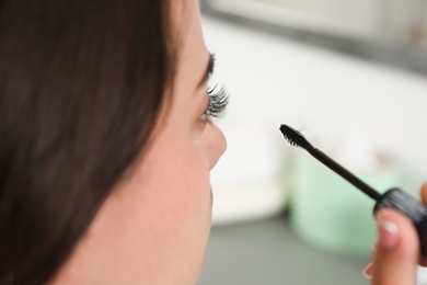 Photo of Young woman holding mascara brush with fallen eyelashes indoors