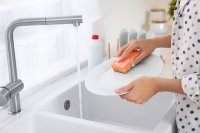 Photo of Woman washing plate above sink in modern kitchen, closeup