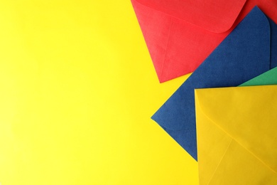 Colorful paper envelopes on yellow background, top view. Space for text