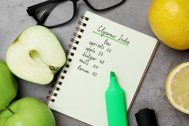 Notebook with products of low glycemic index, marker, glasses and fresh fruits on grey table, flat lay