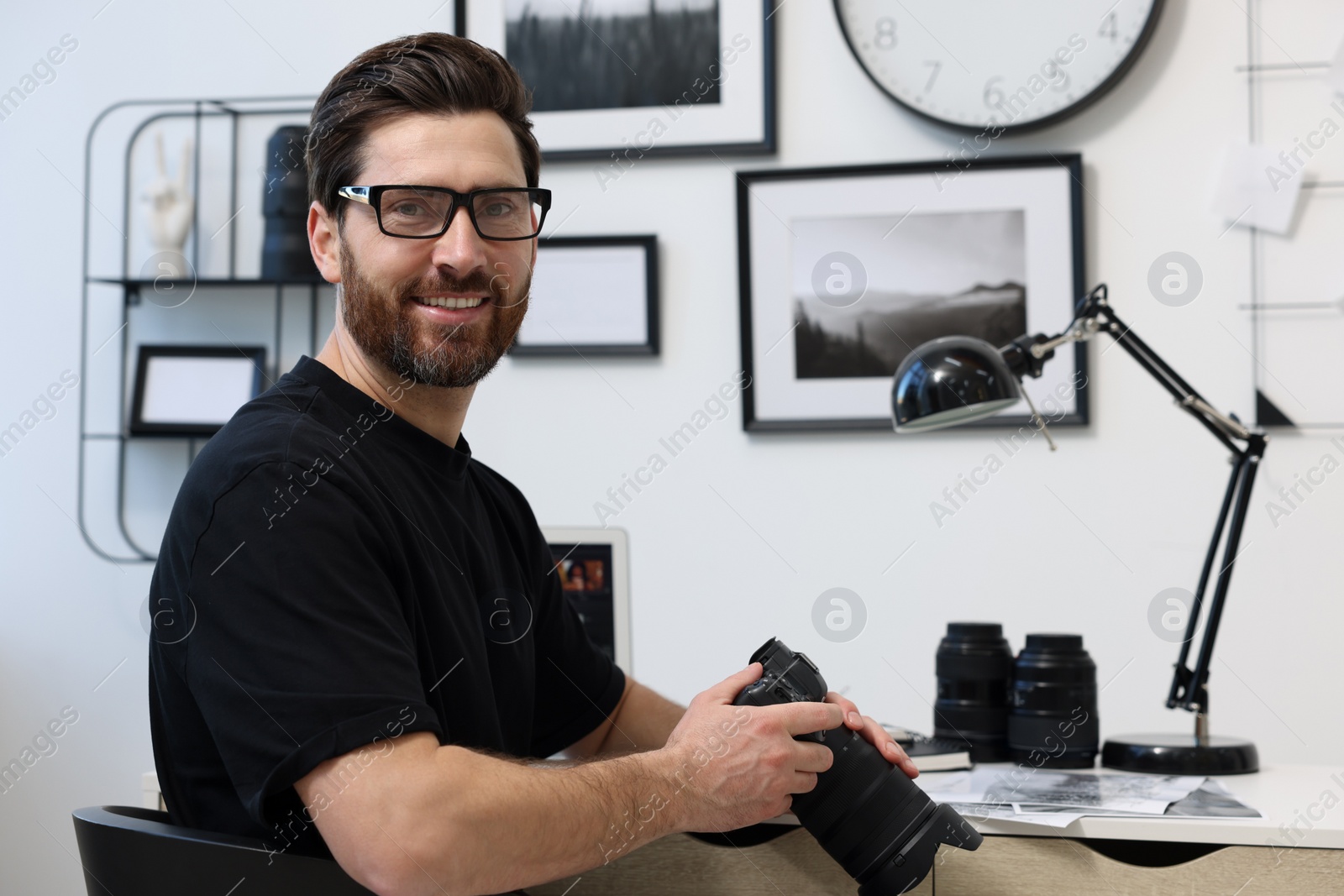 Photo of Professional photographer in glasses holding digital camera at table in office